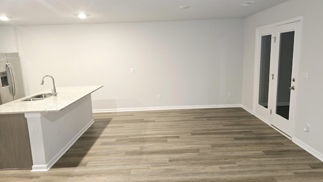 kitchen with a kitchen island with sink, stainless steel refrigerator with ice dispenser, sink, light stone countertops, and dark hardwood / wood-style flooring