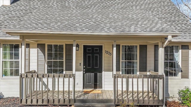 doorway to property with covered porch and a shingled roof