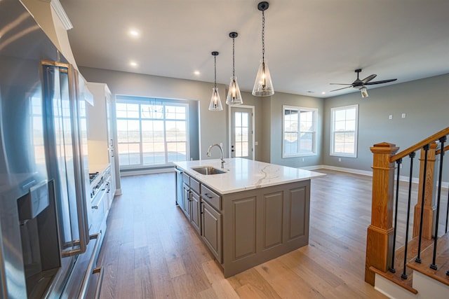 kitchen with light stone counters, sink, refrigerator with ice dispenser, a center island with sink, and gray cabinets