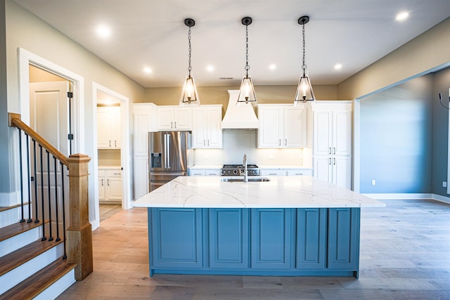 kitchen featuring pendant lighting, a large island with sink, sink, stainless steel fridge, and light stone countertops