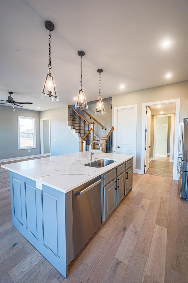 kitchen featuring light stone counters, stainless steel appliances, a kitchen island with sink, sink, and decorative light fixtures