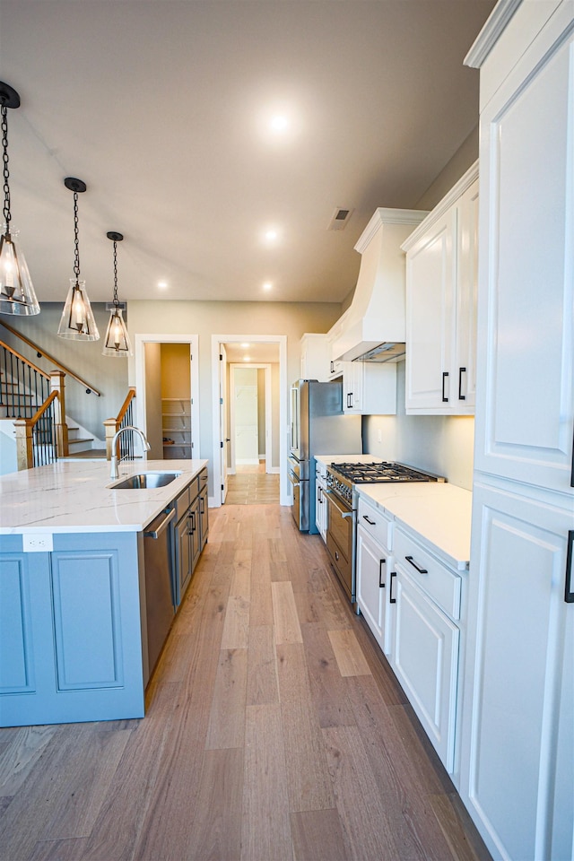 kitchen featuring premium range hood, white cabinetry, hanging light fixtures, and sink