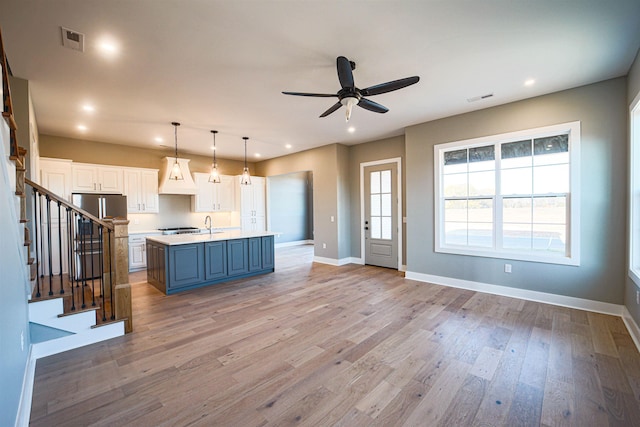 kitchen featuring blue cabinetry, light hardwood / wood-style flooring, pendant lighting, a kitchen island with sink, and white cabinets