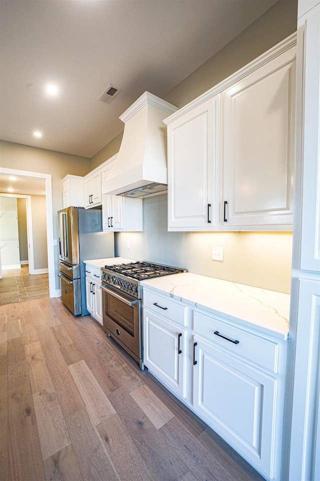 kitchen featuring light stone countertops, appliances with stainless steel finishes, light wood-type flooring, custom range hood, and white cabinets