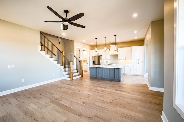 kitchen featuring ceiling fan, premium range hood, stainless steel fridge, an island with sink, and white cabinets