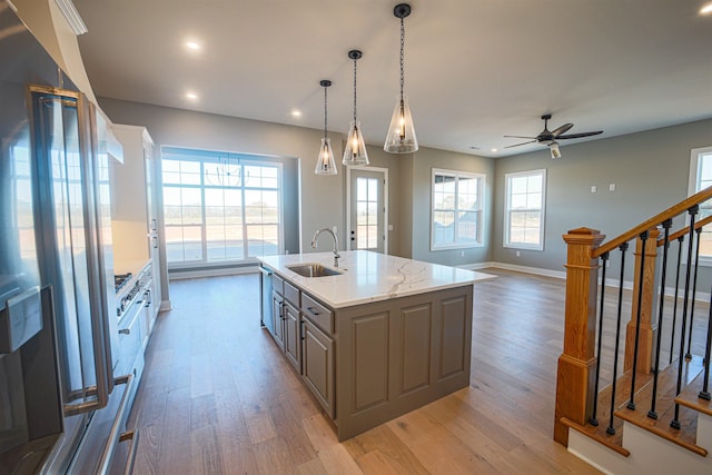 kitchen featuring gray cabinetry, a kitchen island with sink, sink, ceiling fan, and light stone countertops