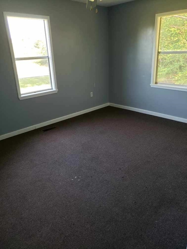 unfurnished room with visible vents, dark carpet, and baseboards