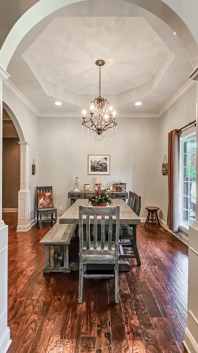 dining space with decorative columns, ornamental molding, a tray ceiling, dark wood-type flooring, and a notable chandelier