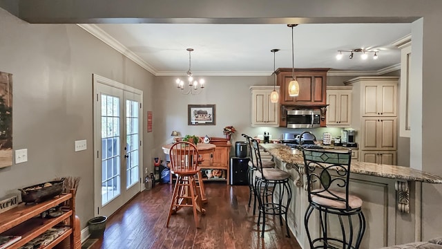 kitchen featuring light stone countertops, hanging light fixtures, cream cabinets, a kitchen bar, and appliances with stainless steel finishes