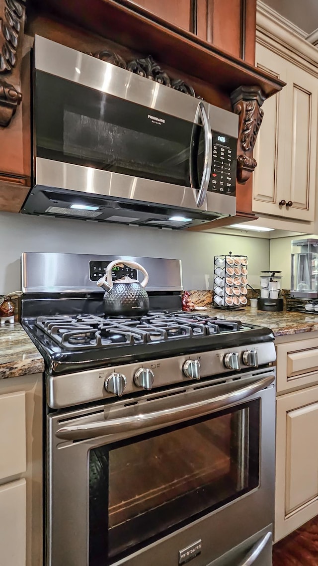 kitchen featuring light stone countertops, stainless steel appliances, and cream cabinetry