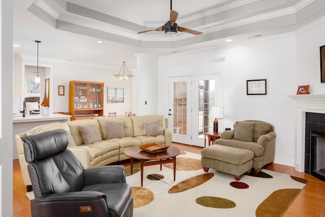 living area with visible vents, a tiled fireplace, light wood finished floors, a raised ceiling, and ceiling fan