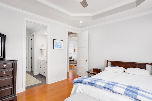 bedroom with a raised ceiling, light wood-style flooring, connected bathroom, crown molding, and baseboards