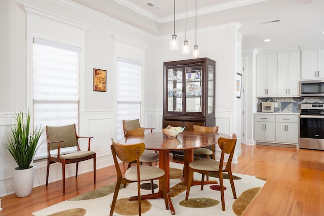 dining area featuring visible vents, light wood finished floors, wainscoting, crown molding, and a decorative wall