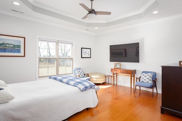 bedroom with a tray ceiling, wood finished floors, and visible vents