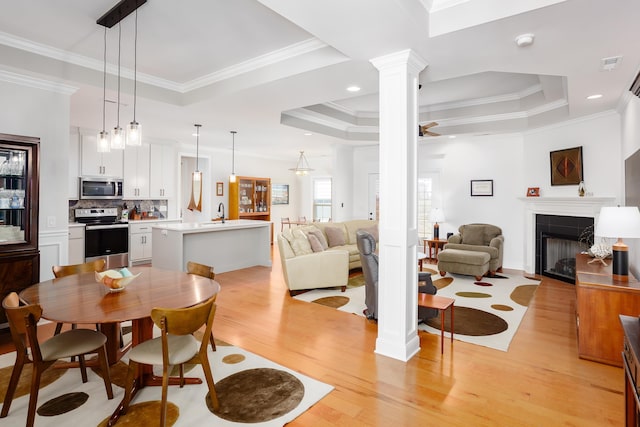 dining space featuring a tiled fireplace, light wood-type flooring, a tray ceiling, ornamental molding, and decorative columns