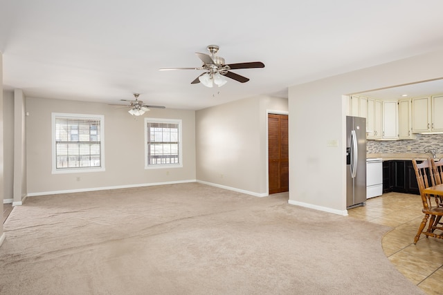 living area featuring light tile patterned floors, ceiling fan, baseboards, and light colored carpet