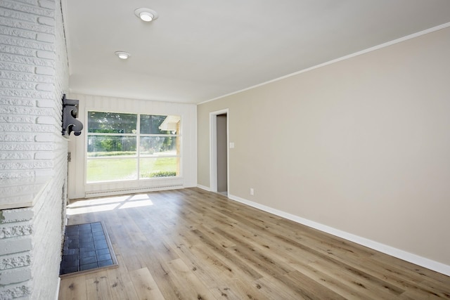 empty room with light hardwood / wood-style floors, a brick fireplace, and crown molding