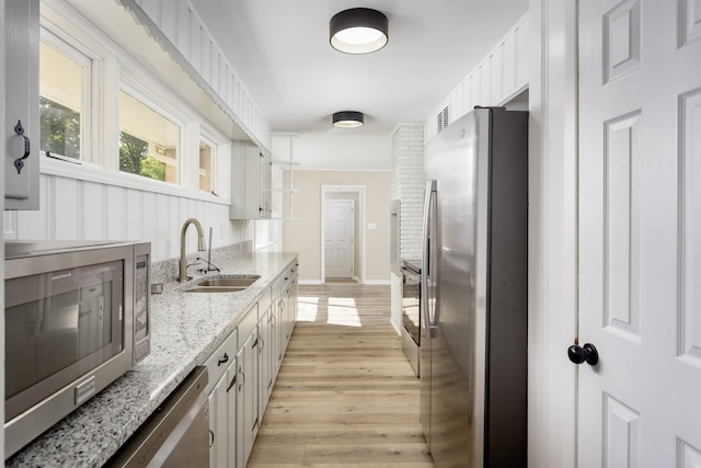 kitchen with appliances with stainless steel finishes, light wood-type flooring, light stone counters, sink, and white cabinetry