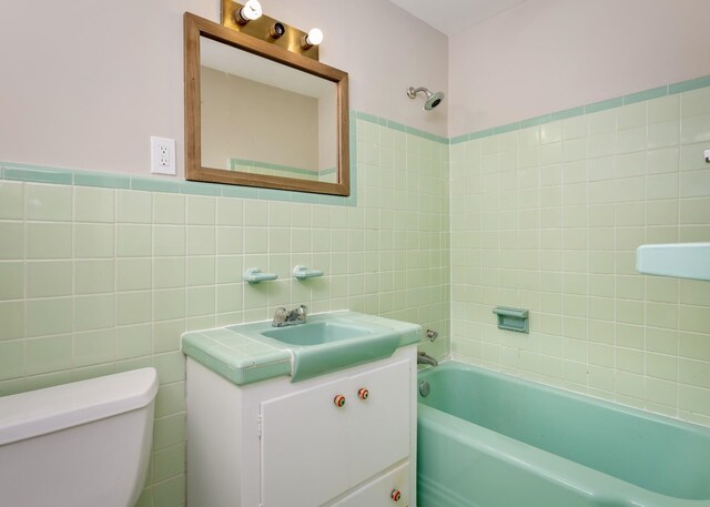 full bathroom featuring tiled shower / bath, vanity, tile walls, and toilet