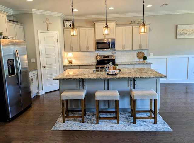  - kitchen featuring appliances with stainless steel finishes, dark wood-style floors, a kitchen breakfast bar, ornamental molding, and a center island with sink
