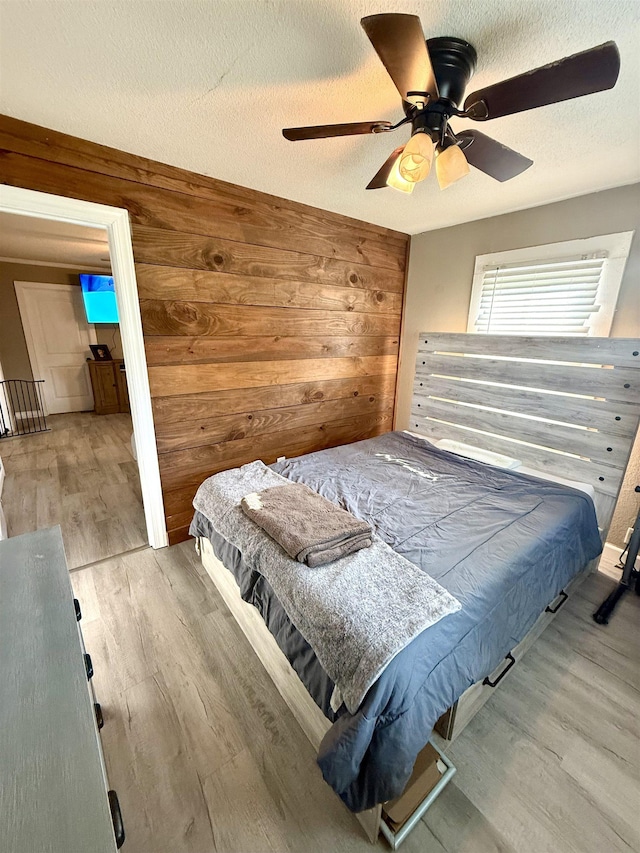  - bedroom featuring wood finished floors, wooden walls, a ceiling fan, and a textured ceiling