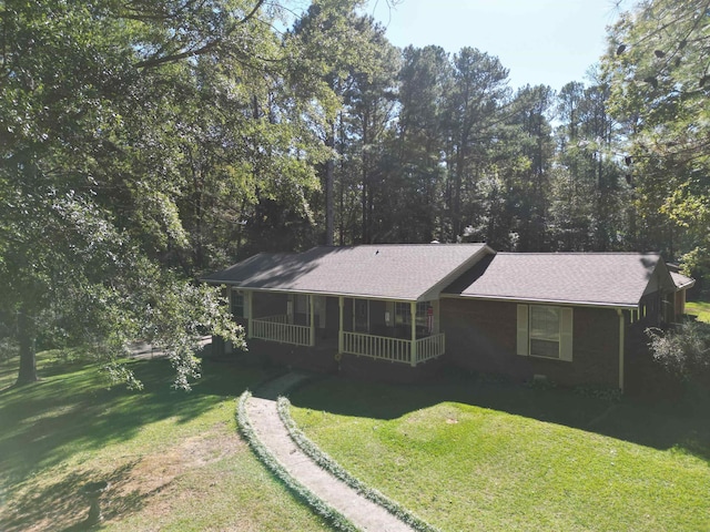 view of front of house featuring roof with shingles, covered porch, and a front lawn