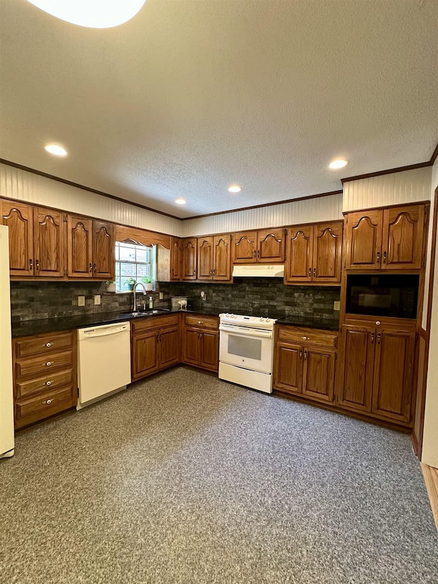 kitchen featuring dark countertops, brown cabinets, a sink, under cabinet range hood, and white appliances
