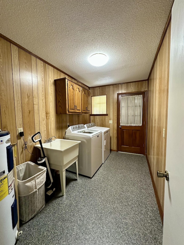 clothes washing area featuring wooden walls, washer and clothes dryer, water heater, and cabinet space