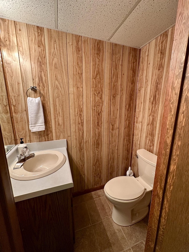 half bath featuring toilet, tile patterned floors, wood walls, and vanity