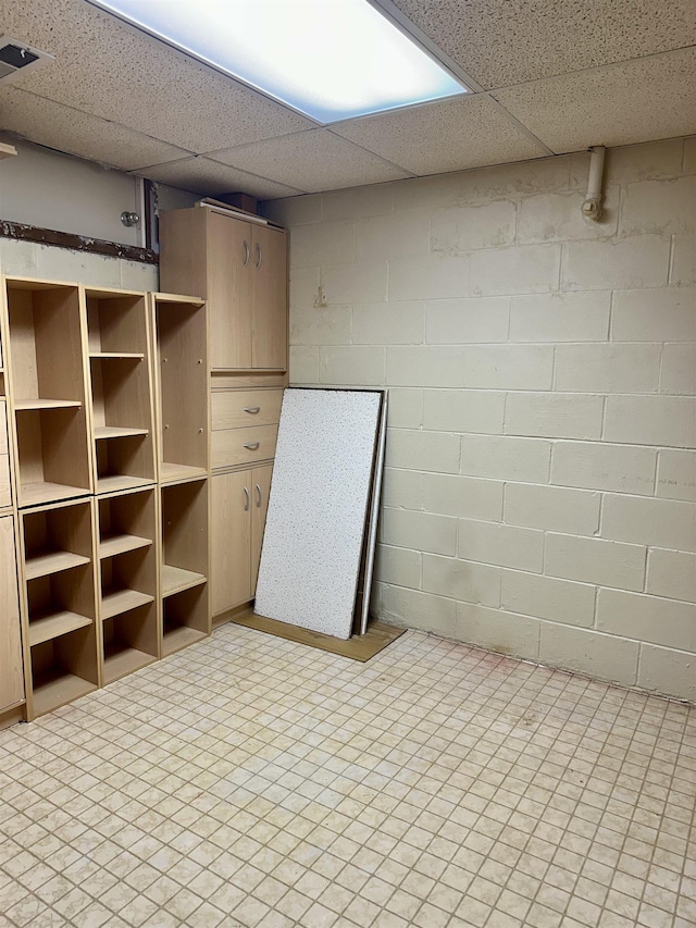 finished below grade area with concrete block wall, visible vents, and a paneled ceiling