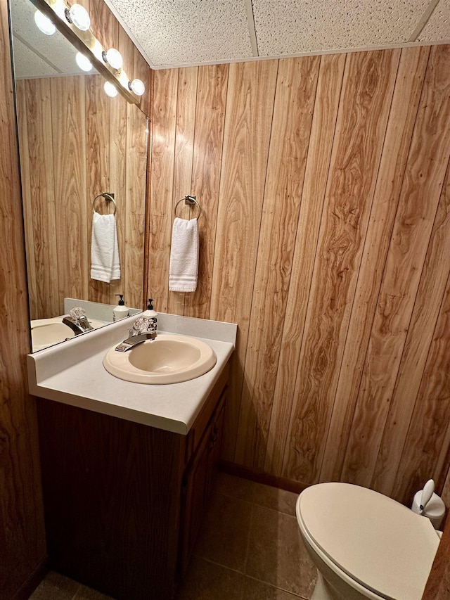 bathroom featuring toilet, wood walls, tile patterned flooring, and vanity