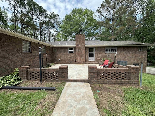 back of house featuring brick siding, central AC, a chimney, and a patio area