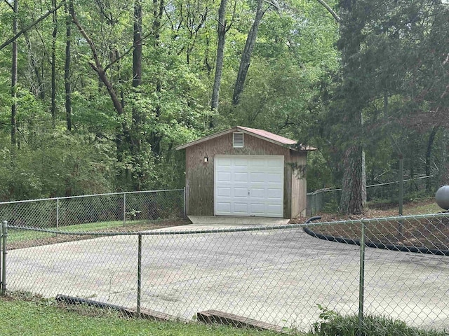 detached garage featuring a view of trees, fence, and driveway