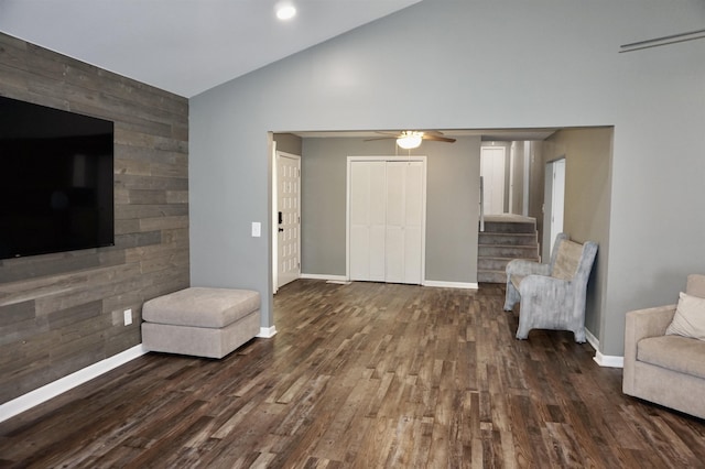 living area with wooden walls, ceiling fan, dark wood-type flooring, and vaulted ceiling