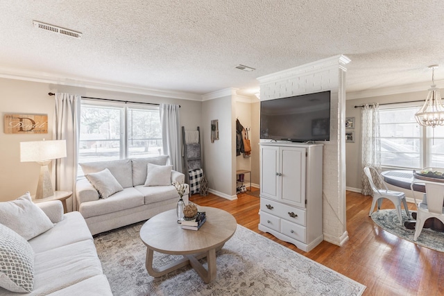 living room with a wealth of natural light, visible vents, a notable chandelier, and light wood-style flooring