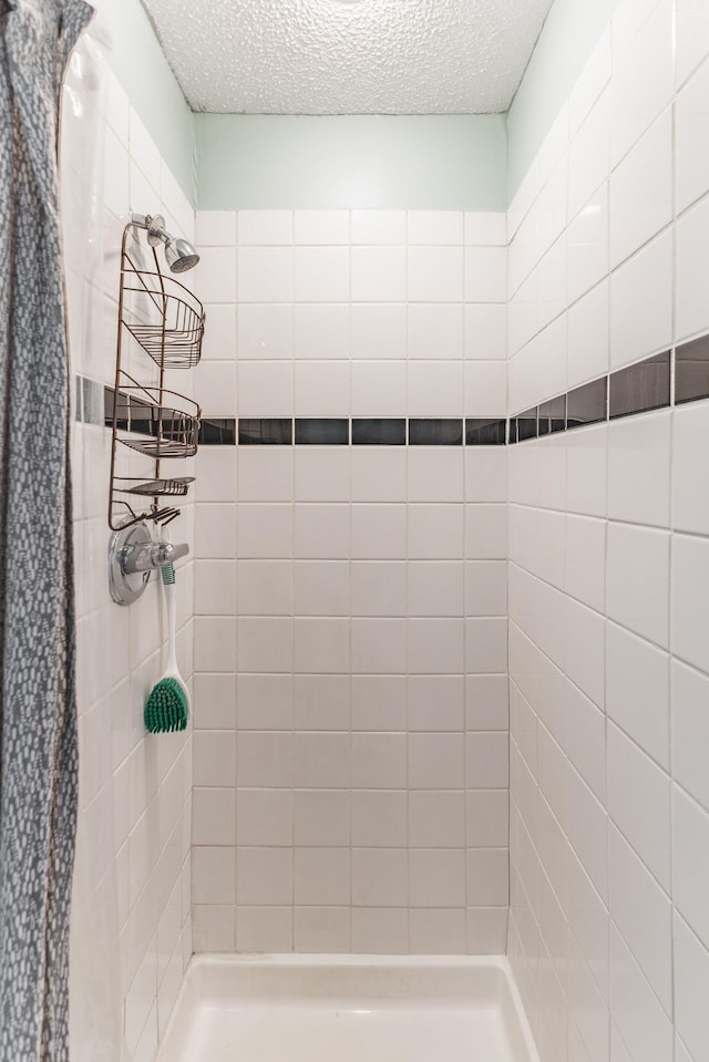 bathroom with a textured ceiling and tiled shower