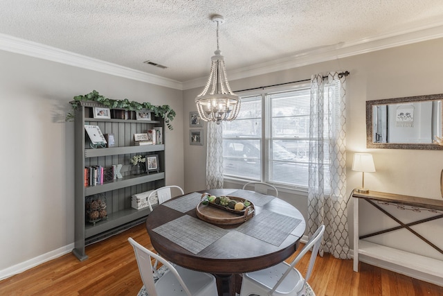 dining area featuring crown molding, visible vents, a textured ceiling, wood finished floors, and a chandelier