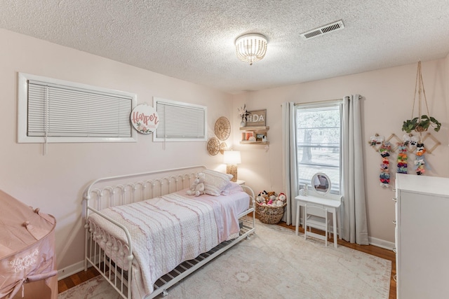 bedroom with baseboards, visible vents, light wood-style flooring, and a textured ceiling