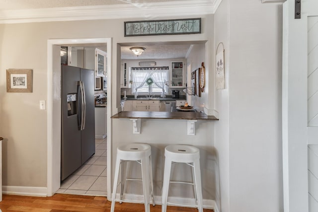 kitchen with a peninsula, a kitchen breakfast bar, ornamental molding, black refrigerator with ice dispenser, and dark countertops