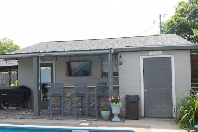  - back of property with concrete block siding, a patio, a shingled roof, and an outdoor pool