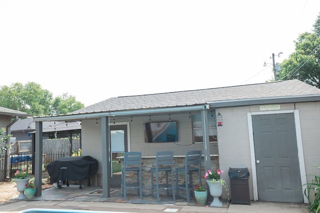 - back of house with concrete block siding, a patio, and roof with shingles