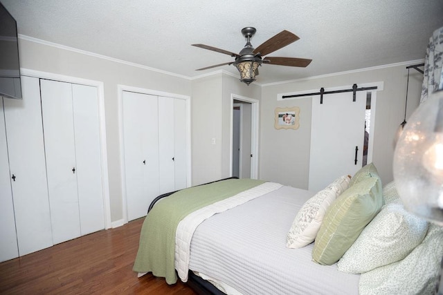  - bedroom featuring wood finished floors, a barn door, two closets, crown molding, and a ceiling fan