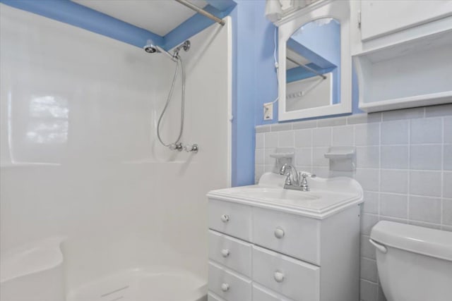 bathroom featuring a shower, vanity, toilet, and tile walls