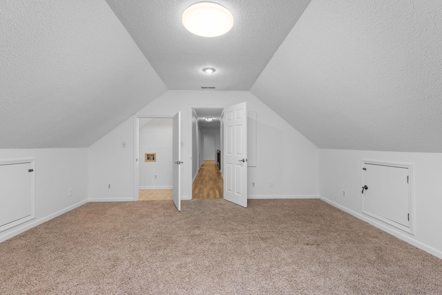 additional living space featuring light colored carpet, lofted ceiling, and a textured ceiling