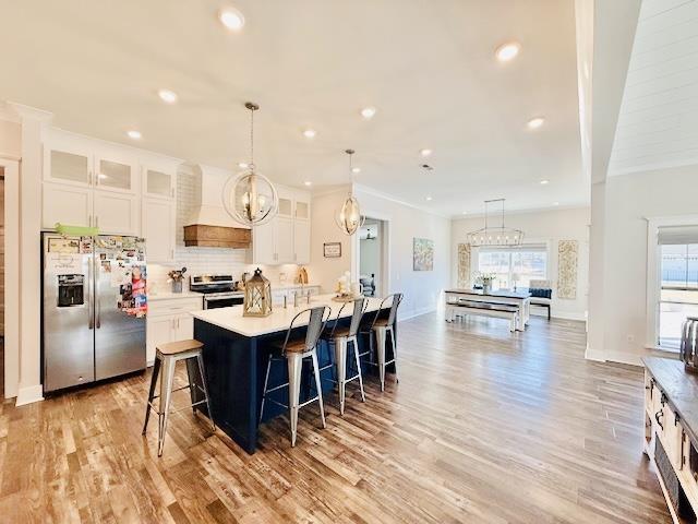  - kitchen featuring stainless steel appliances, custom exhaust hood, light wood finished floors, a breakfast bar area, and white cabinetry