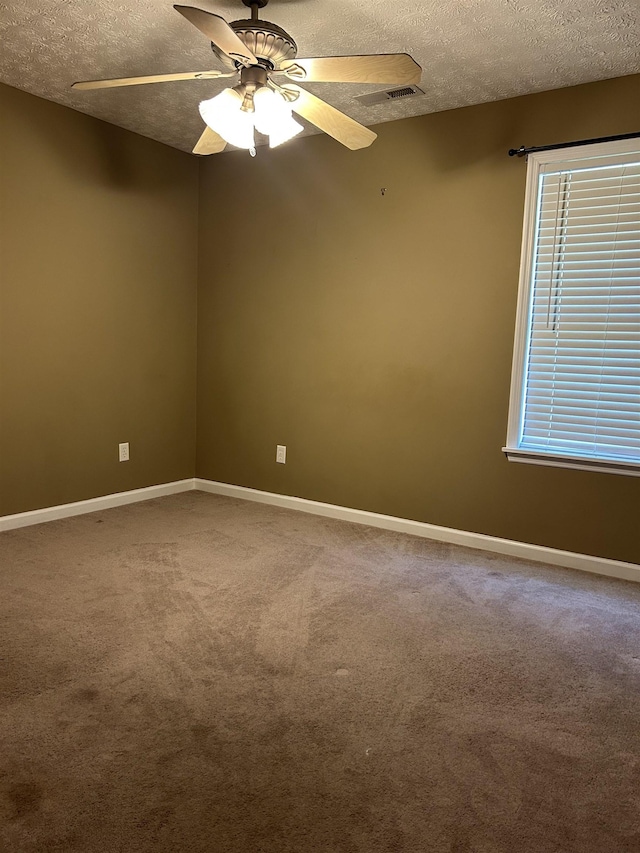 carpeted spare room with baseboards, a textured ceiling, ceiling fan, and a healthy amount of sunlight