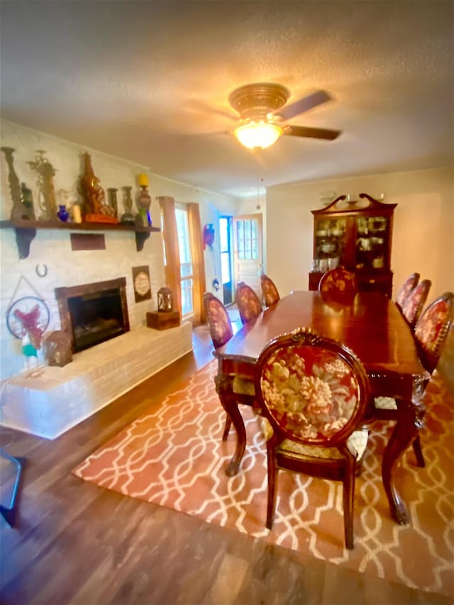 dining space with ceiling fan, a fireplace, hardwood / wood-style floors, and a textured ceiling