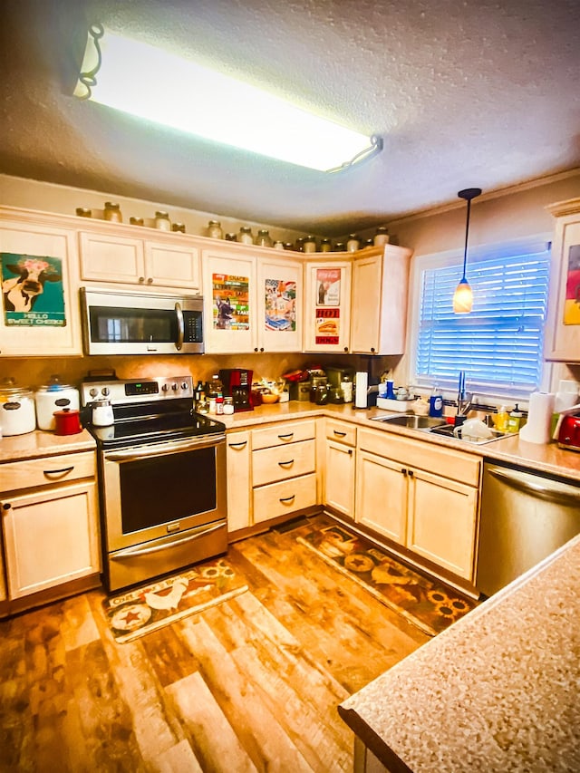 kitchen featuring appliances with stainless steel finishes, light wood-type flooring, a textured ceiling, sink, and hanging light fixtures