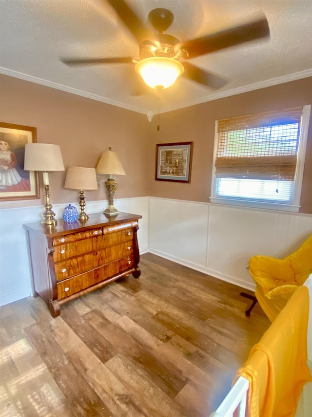 living area featuring ceiling fan, light hardwood / wood-style flooring, a textured ceiling, and ornamental molding