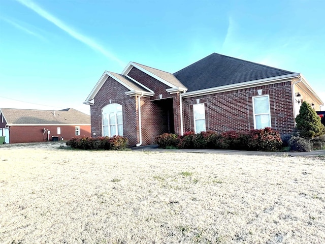 single story home featuring a shingled roof, a front lawn, and brick siding